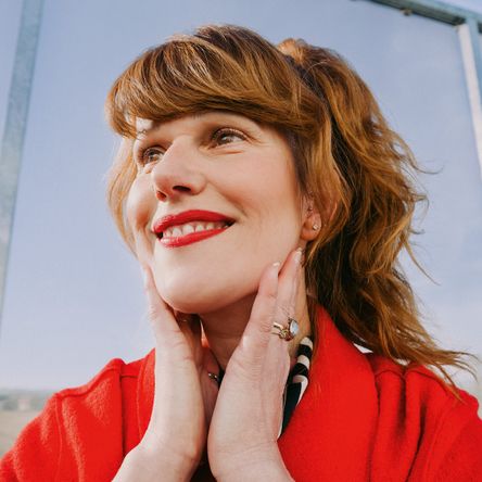 Usmívající se žena v červeném outfitu vyjadřuje sebevědomí a pozitivní energii. Fotka ke kampani Práce mění život