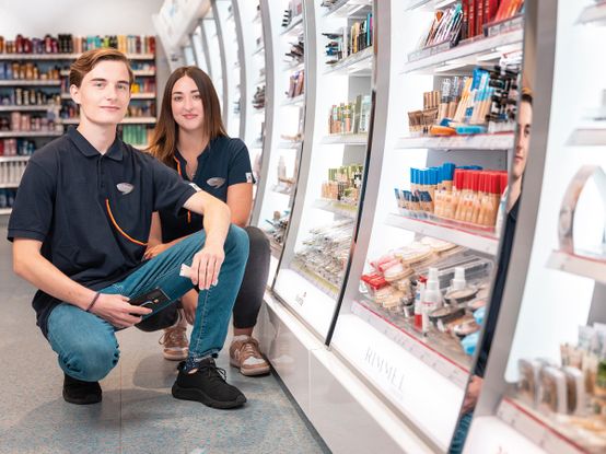 mladý kolega s kolegyní v podřepu u dekorativní kosmetiky