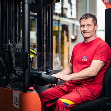 Spolupracovník sedí ve vozíku mezi regály.