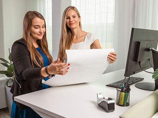 Dvě ženy stojí u stolu a diskutují nad dokumentem