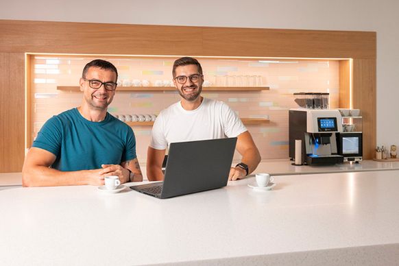 Dva muži, spolupracovníci stojí u stolu v coffe pointu, dívají se do notebooku .