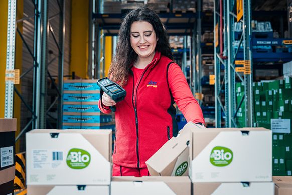 Žena stojí ve skladu u krabic a scanuje produkty dm.